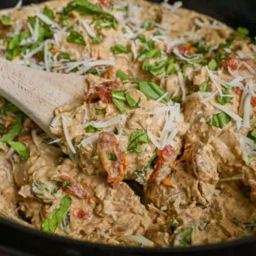 close up of marry me chicken in a crock pot, covered in basil and parmesan, with a spoon.
