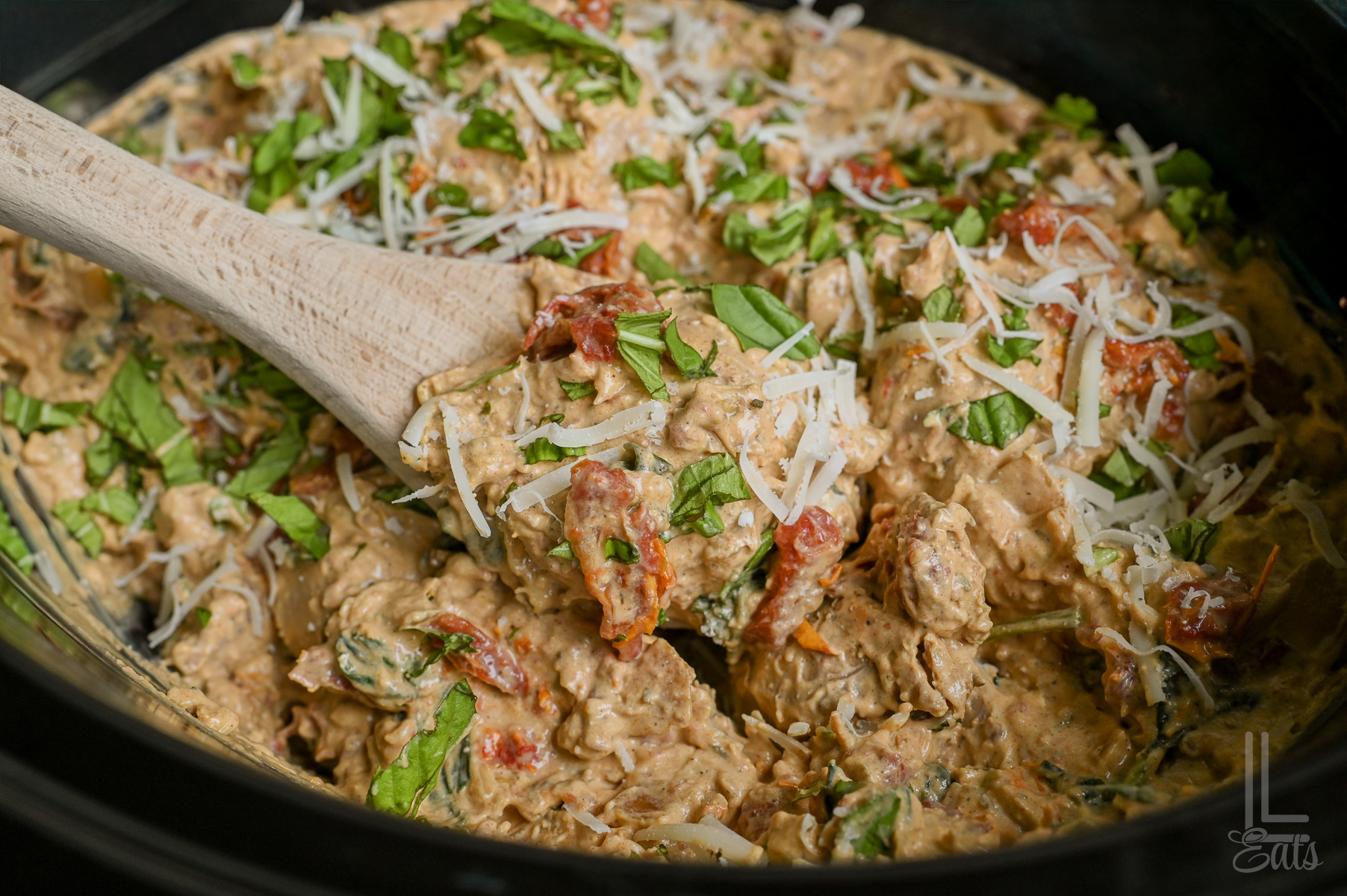 close up of marry me chicken in a crock pot, covered in basil and parmesan, with a spoon.