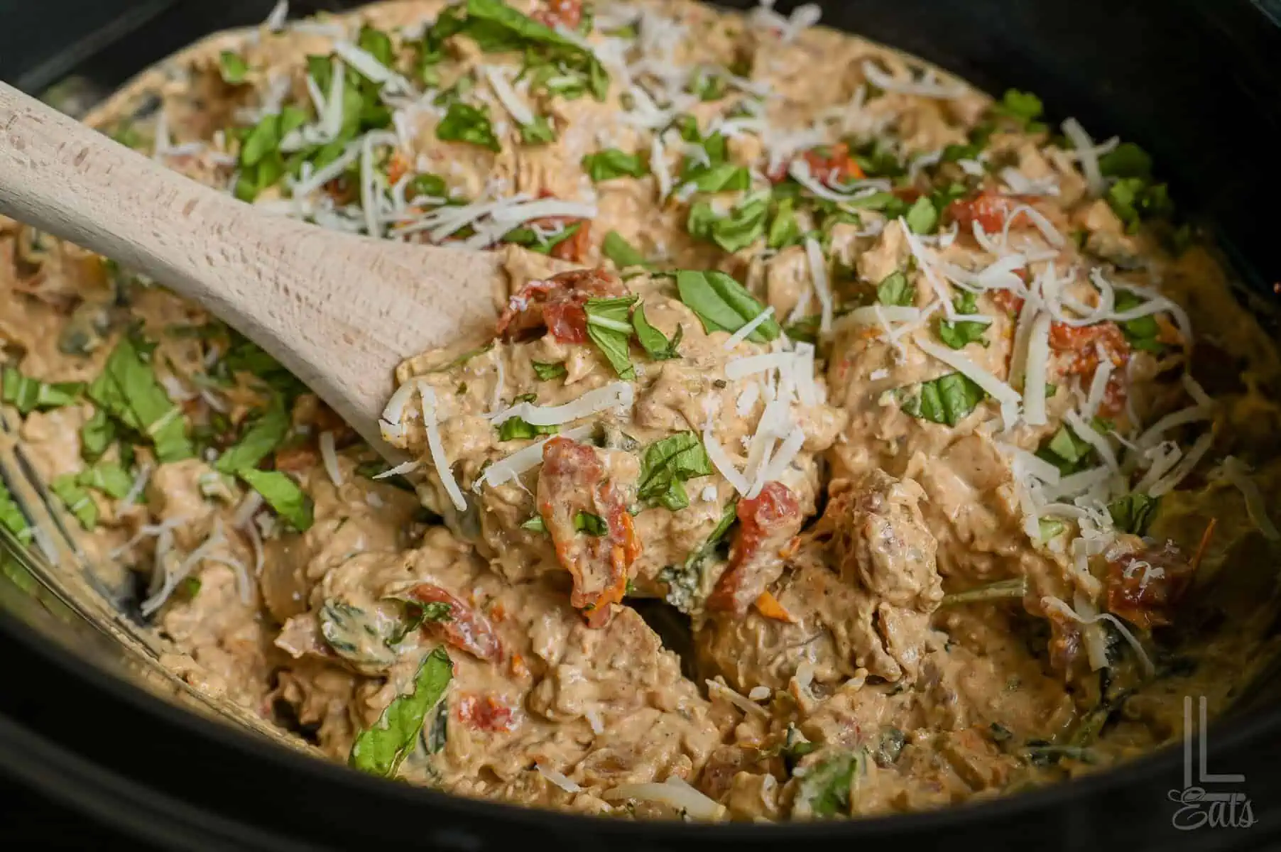 close up of marry me chicken in a crock pot, covered in basil and parmesan, with a spoon.