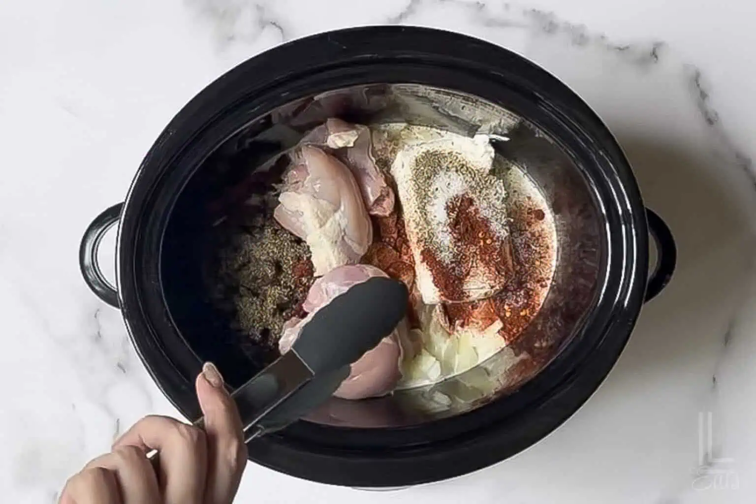 adding boneless chicken thighs to cream cheese, cream, onions, and tomatoes in a slow cooker.