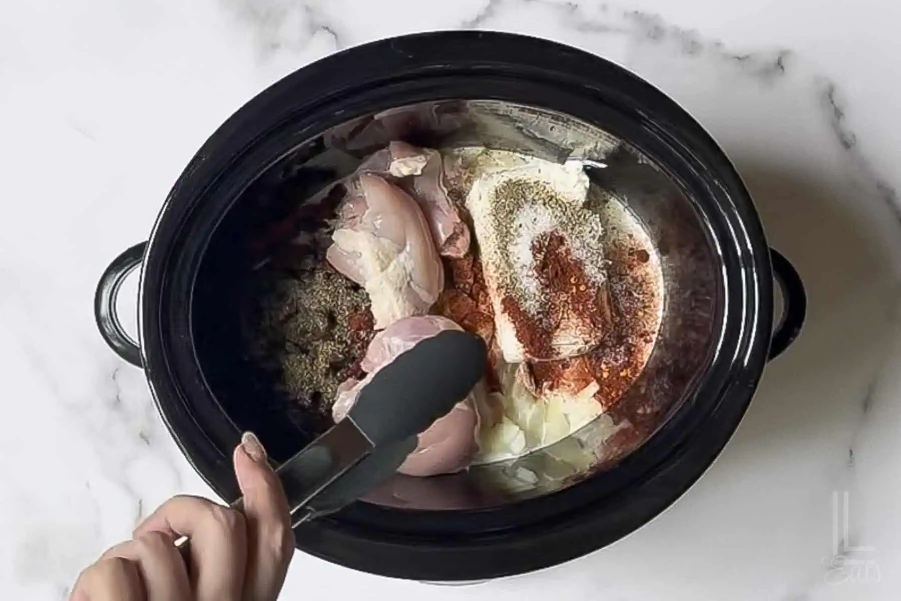 adding boneless chicken thighs to cream cheese, cream, onions, and tomatoes in a slow cooker.