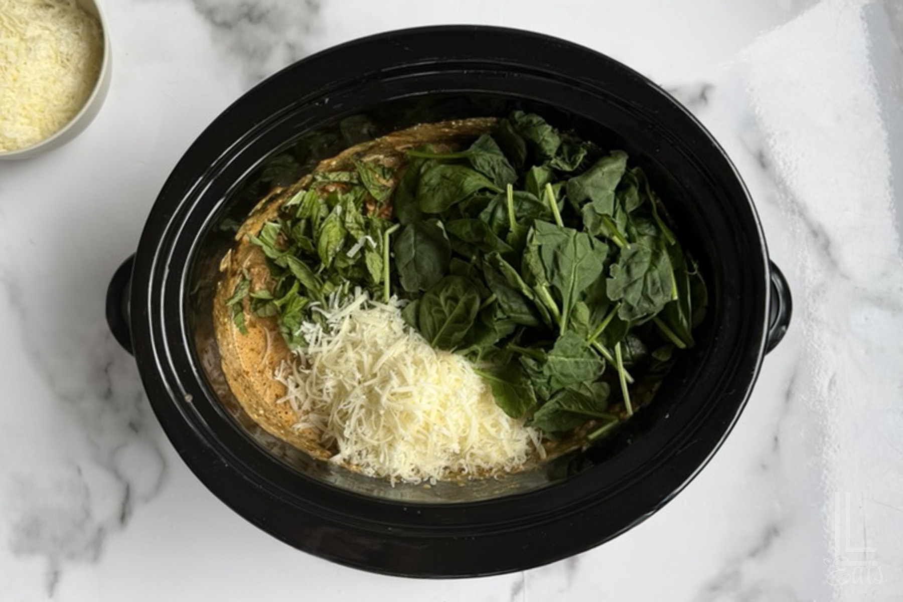 adding spinach, basil, and parmesan to the marry me chicken cooking in the crock pot.
