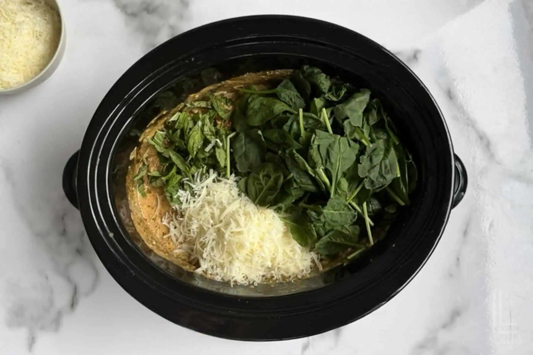 adding spinach, basil, and parmesan to the marry me chicken cooking in the crock pot.