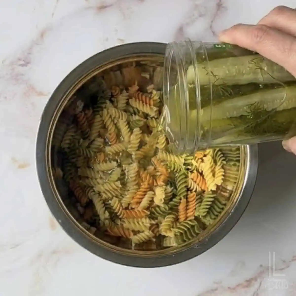 pouring pickle juice over cooked rotini.