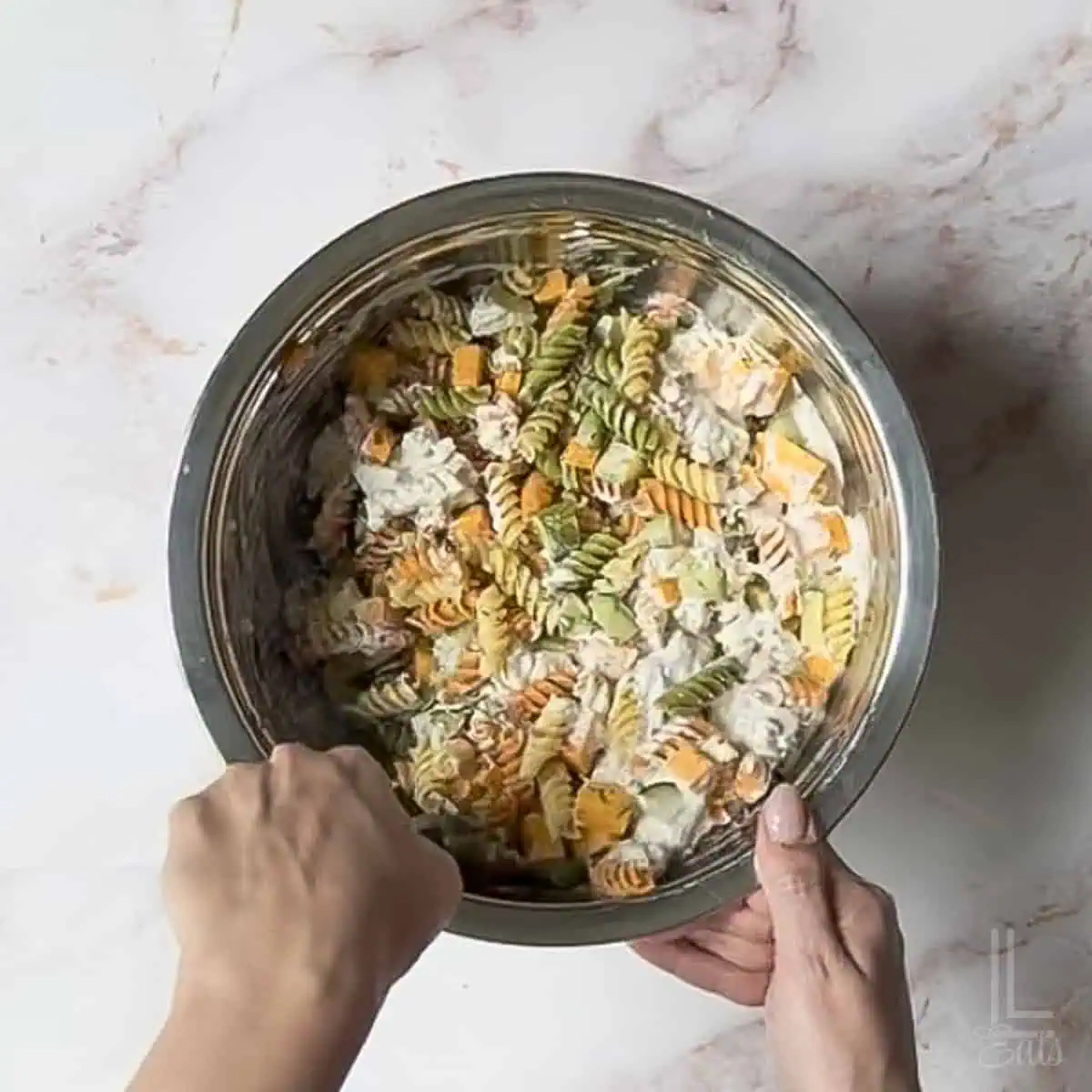 stirring the creamy sauce into the pickle pasta salad.