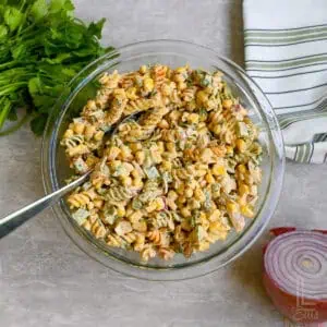 elote pasta salad in a bowl with a spoon, next to red onion, cilantro.
