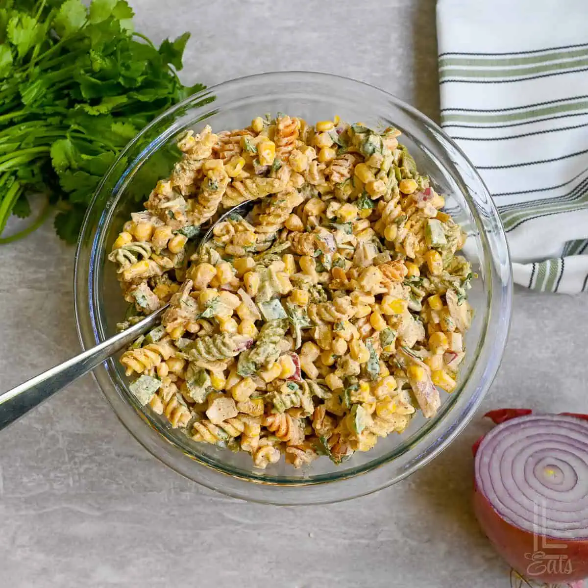 elote pasta salad in a bowl with a spoon, next to red onion, cilantro.