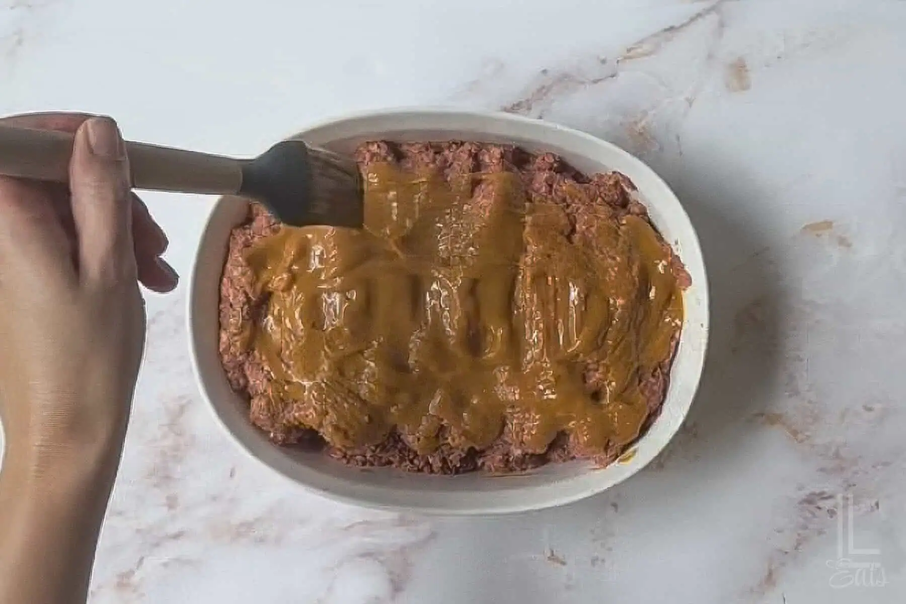 brushing a ketchup/mustard/brown sugar sauce over the uncooked meatloaf.