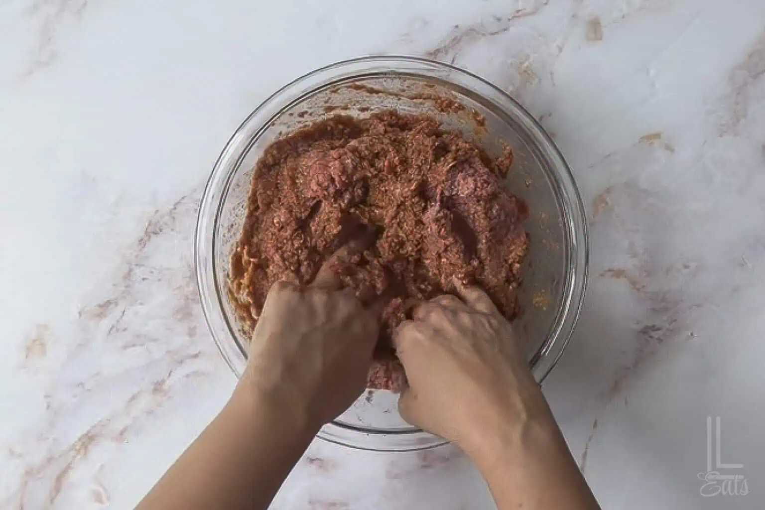 combining the ingredients for the meatloaf with hands.