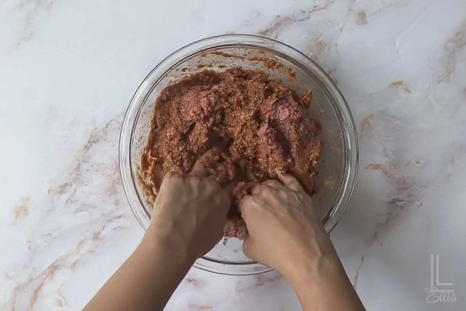 combining the ingredients for the meatloaf with hands.