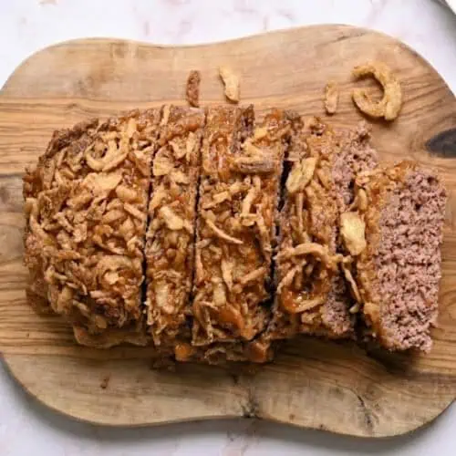 lipton onion soup meatloaf, topped with a brown sugar glaze and crispy fried onions, on a cutting board.