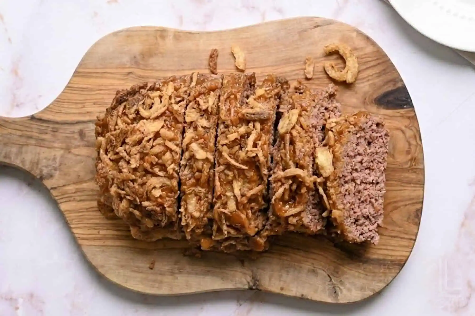 lipton onion soup meatloaf, topped with a brown sugar glaze and crispy fried onions, on a cutting board.