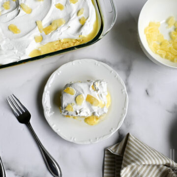 slice of pineapple poke cake on a plate, next to a baking dish.