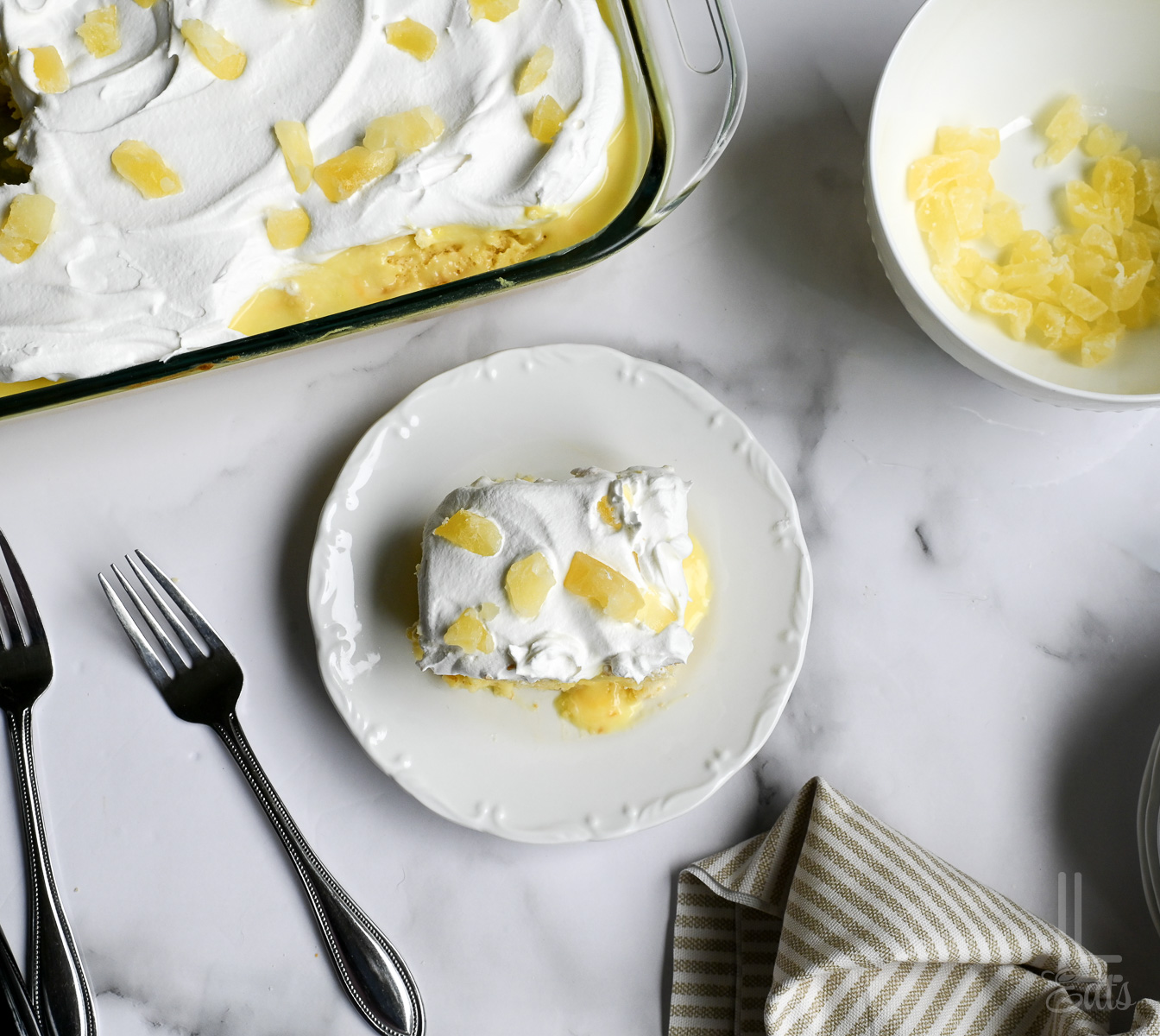 slice of pineapple poke cake on a plate, next to a baking dish.