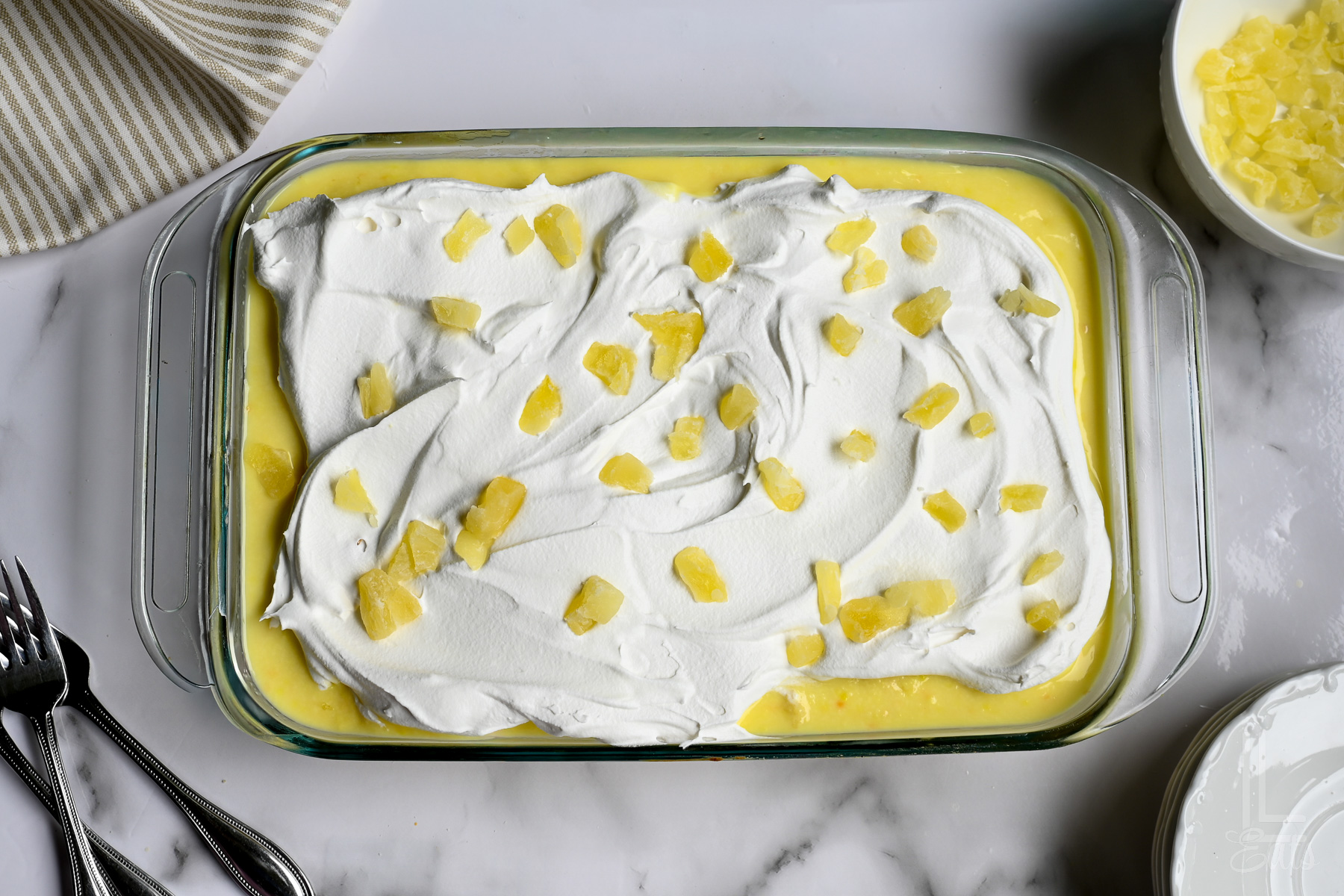 pineapple poke cake topped with whipped cream and dried pineapple pieces.
