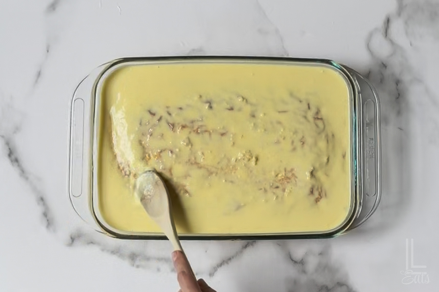 smoothing out the pineapple pudding mixture on the poke cake with a wooden spoon.