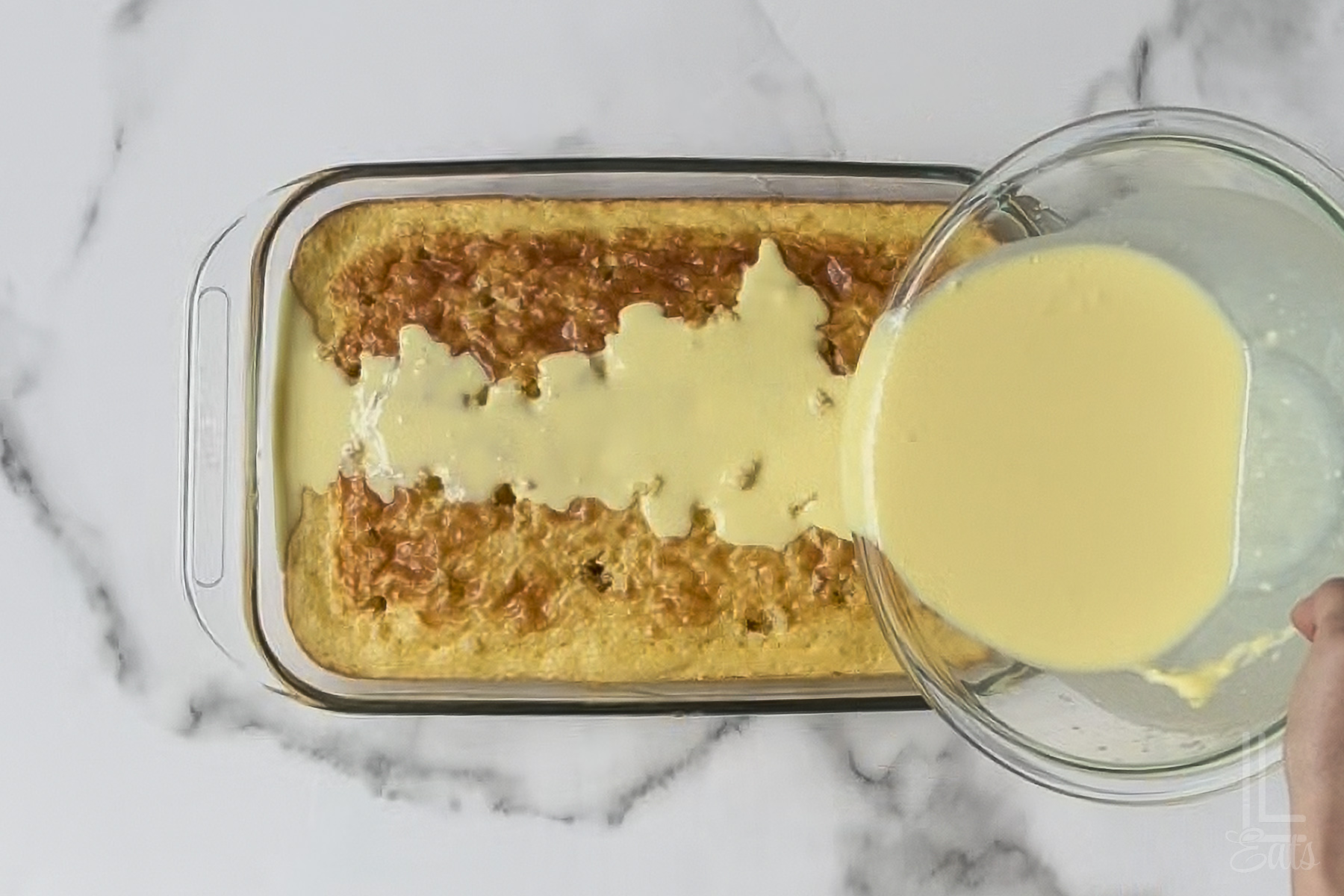 pouring the pineapple pudding mixture over the top of the cake with poked holes.
