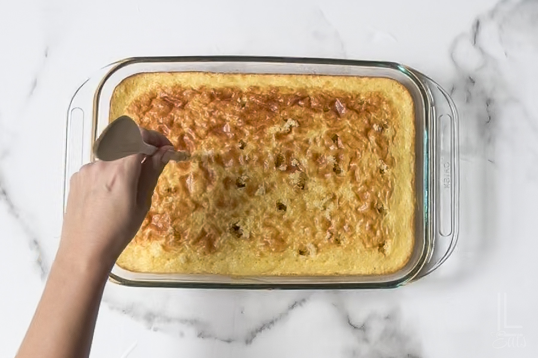 poking holes in the baked pineapple cake with a wooden spoon.