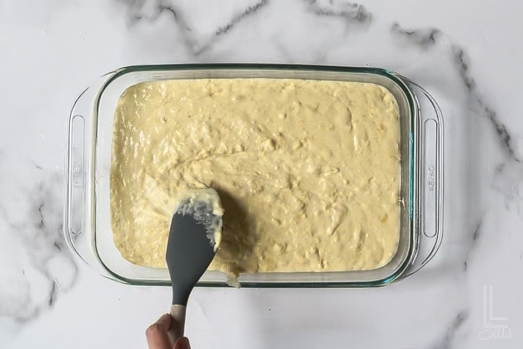 spreading a pineapple cake batter in a 9x13 inch baking dish.