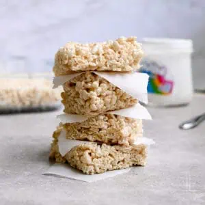 rice krispie treats stacked in front of a baking dish, marshmallow fluff container.