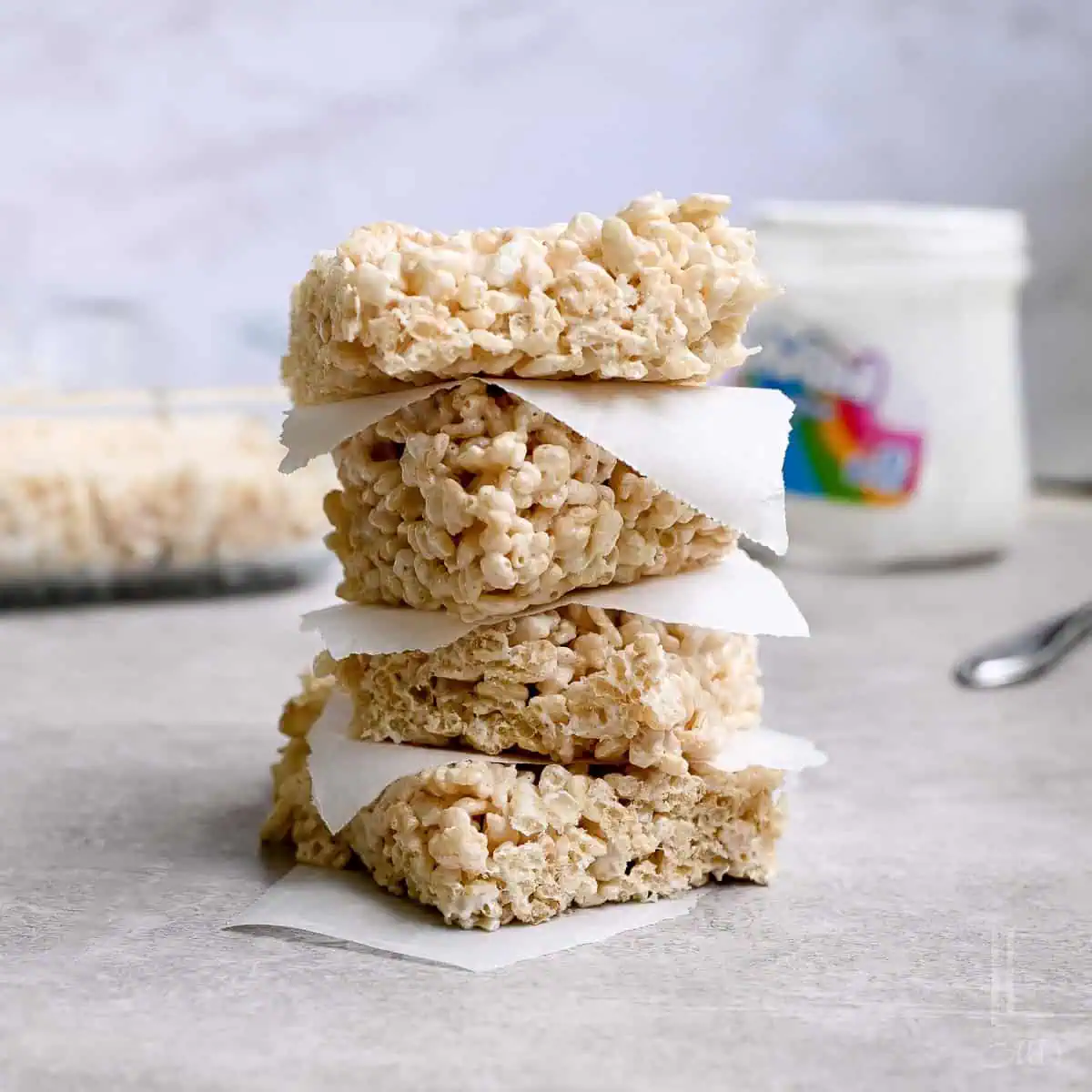 rice krispie treats stacked in front of a baking dish, marshmallow fluff container.