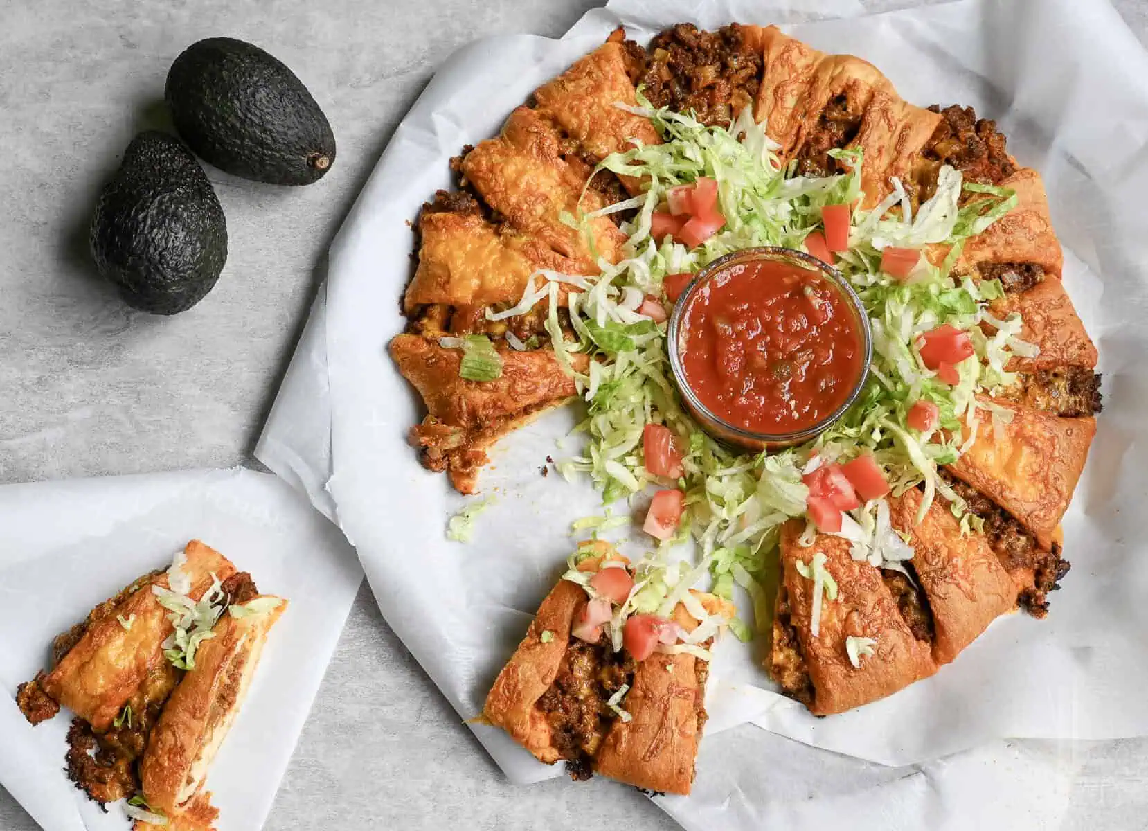 taco crescent ring with pieces cut and removed, garnished with lettuce, tomato, and salsa.