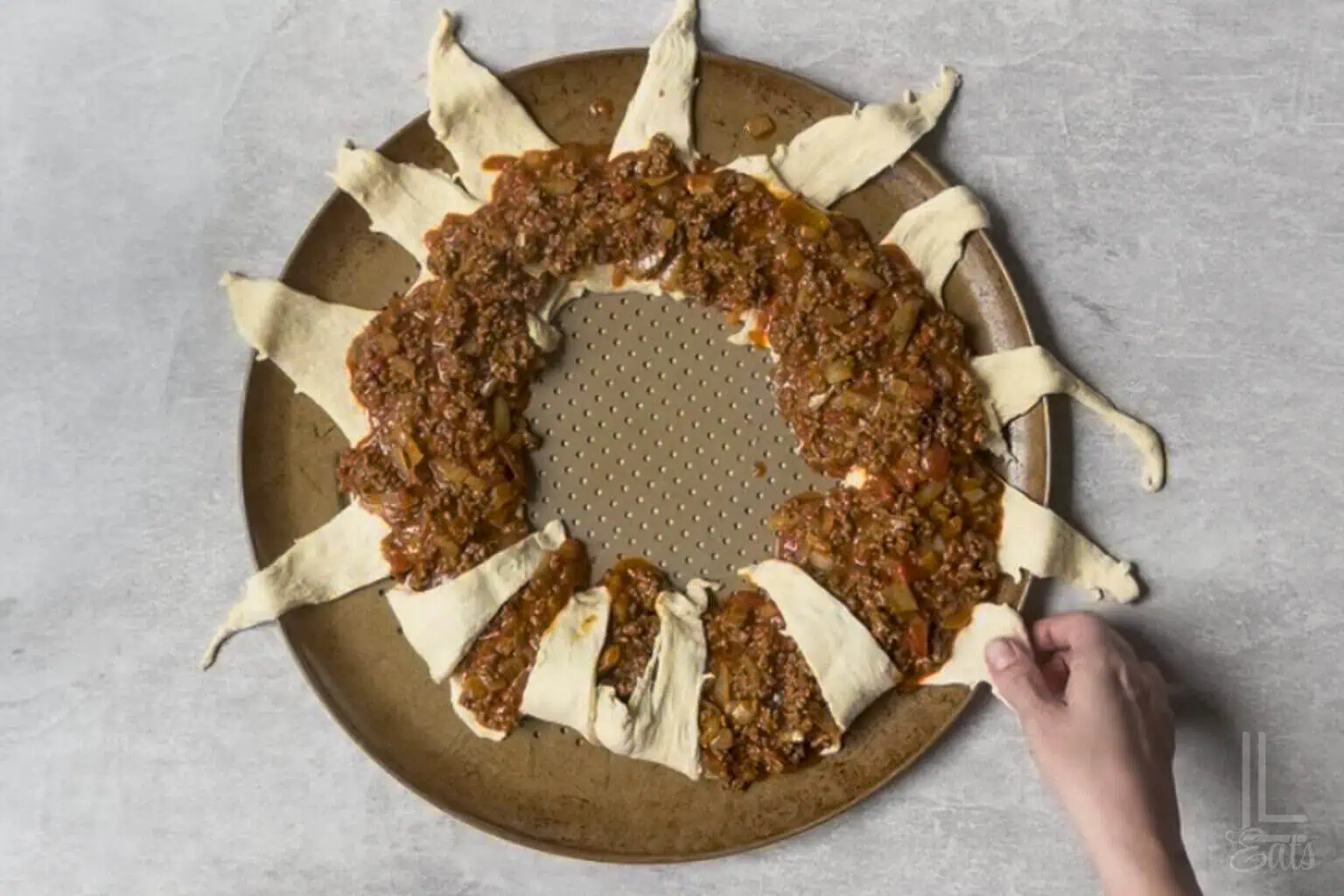 folding the outside pieces of the crescent roll sunburst shape in after covering the inner part in taco meat mixture.