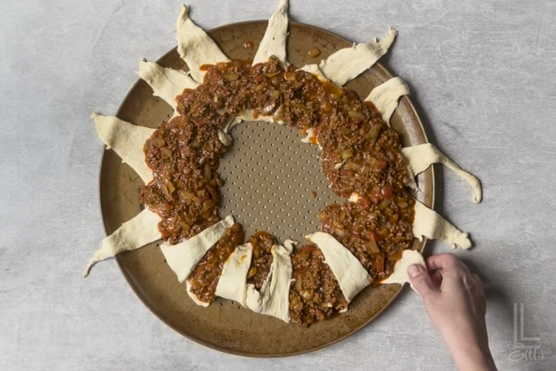 folding the outside pieces of the crescent roll sunburst shape in after covering the inner part in taco meat mixture.