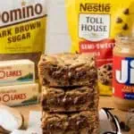 Peanut butter chocolate chip cookie bars with ingredients in the background for dessert recipe.