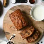 Chocolate chip banana bread slices on a wooden board with milk and baking ingredients.