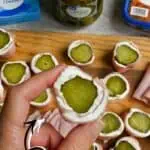 Close-up of homemade pickle roll-ups with cream cheese on a wooden board.