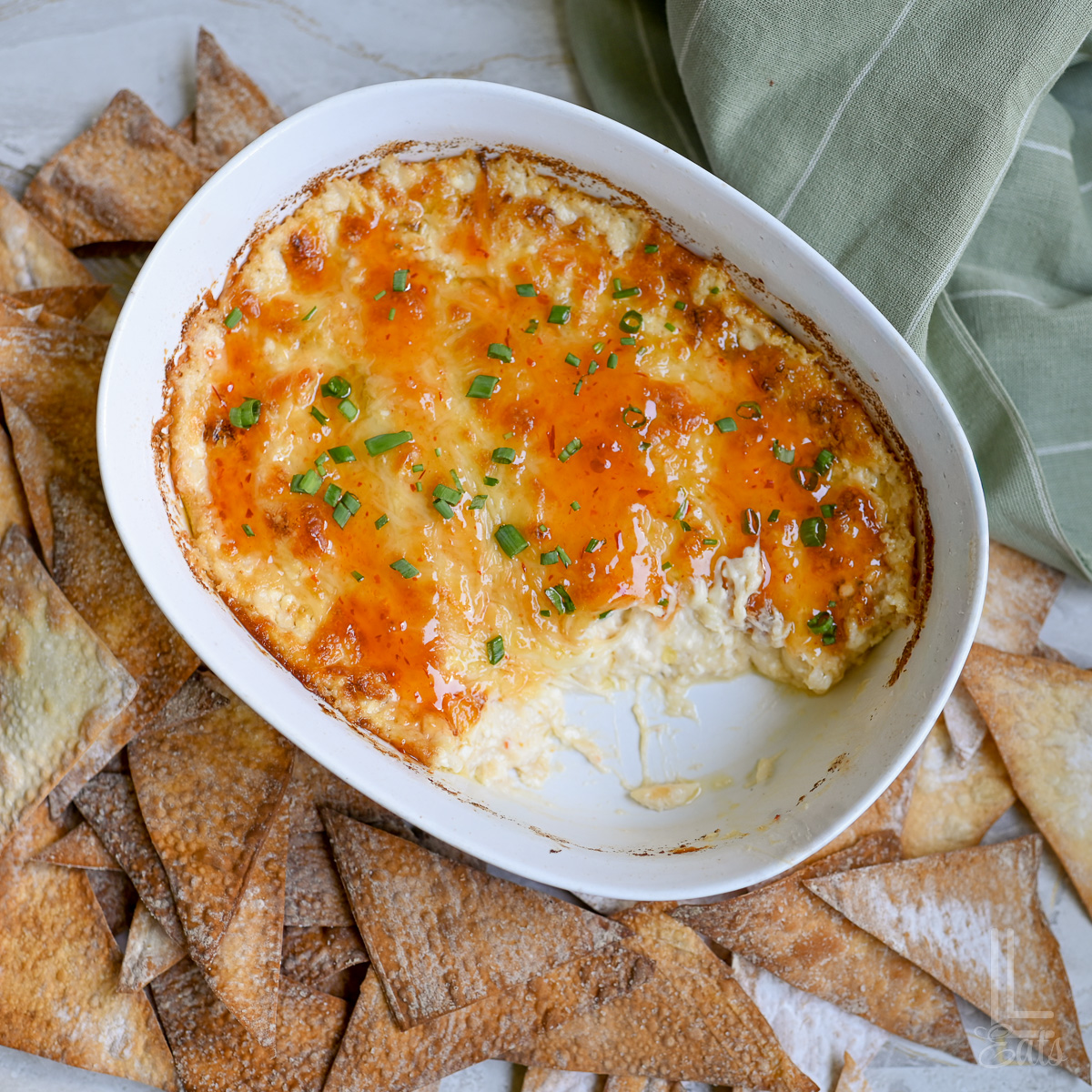 baked crab rangoon dip in an oval dish, covered in sweet chili glaze and green onions, surrounded by baked wonton chips.
