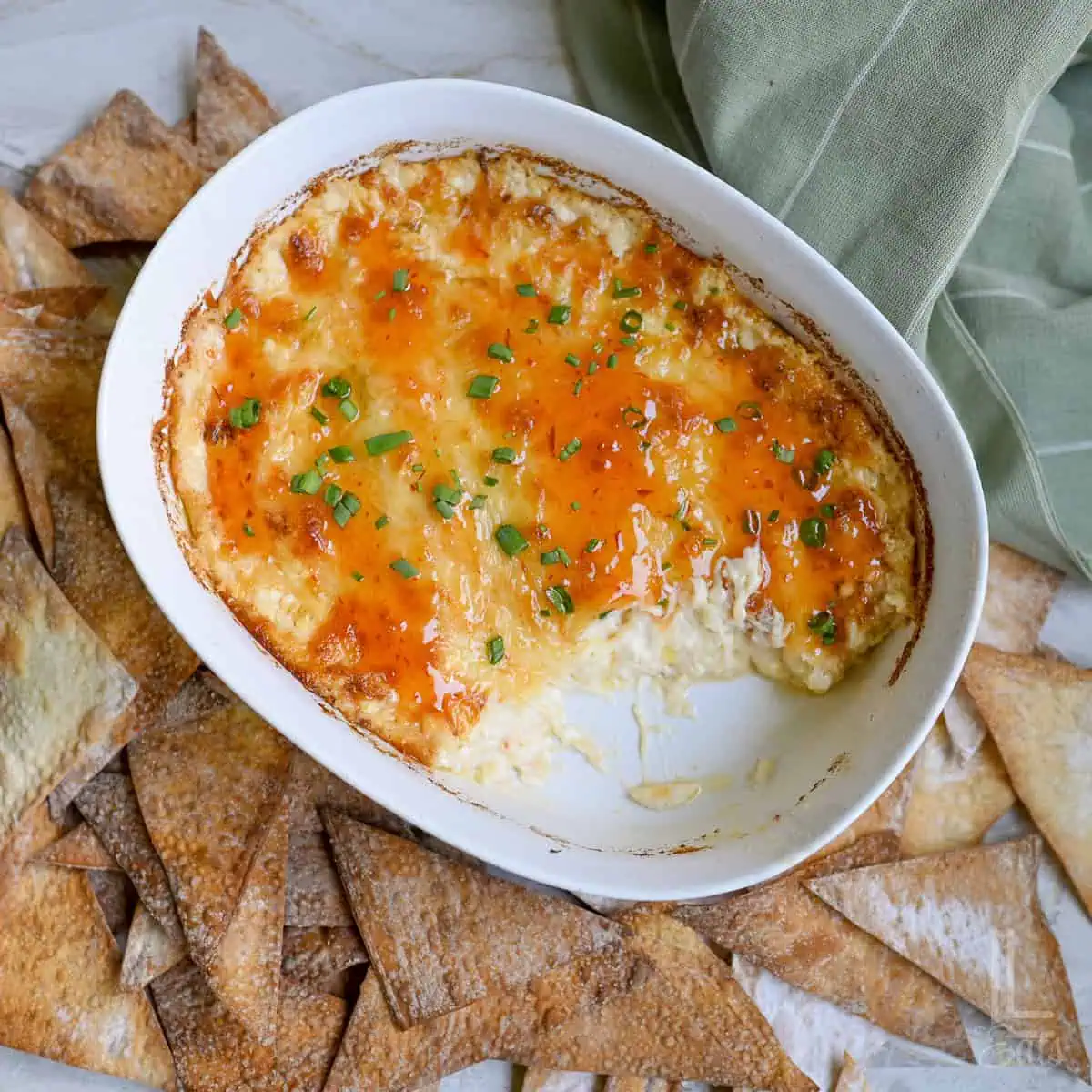 crab rangoon dip in a baking dish, covered in sweet chili glaze and green onions, surrounded by baked wonton chips.