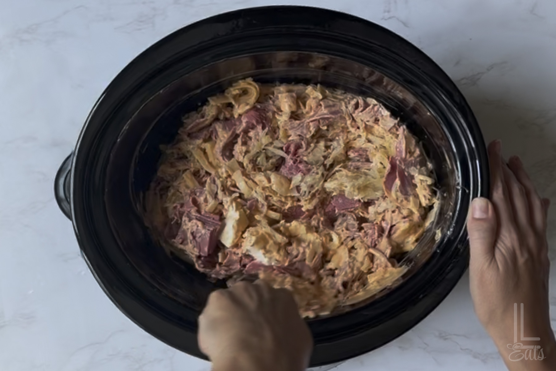 mixing ingredients for reuben dip in an oval slow cooker.