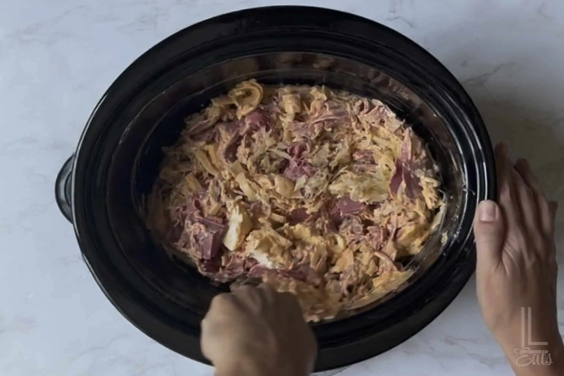 mixing ingredients for reuben dip in an oval slow cooker.