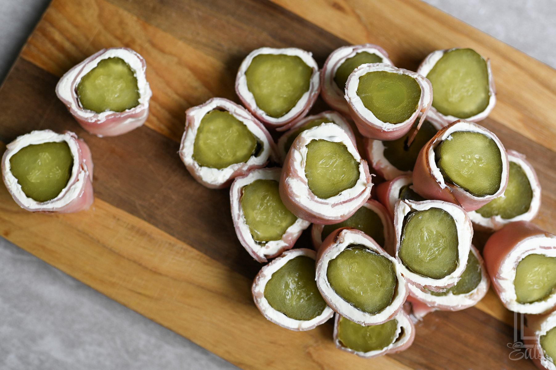 dill pickle roll ups, with ham and cream cheese, on a cutting board.