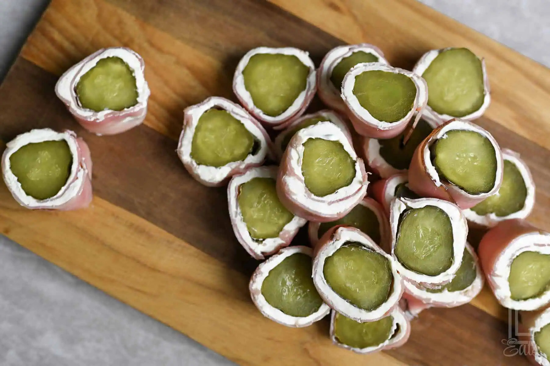 dill pickle roll ups, with ham and cream cheese, on a cutting board.