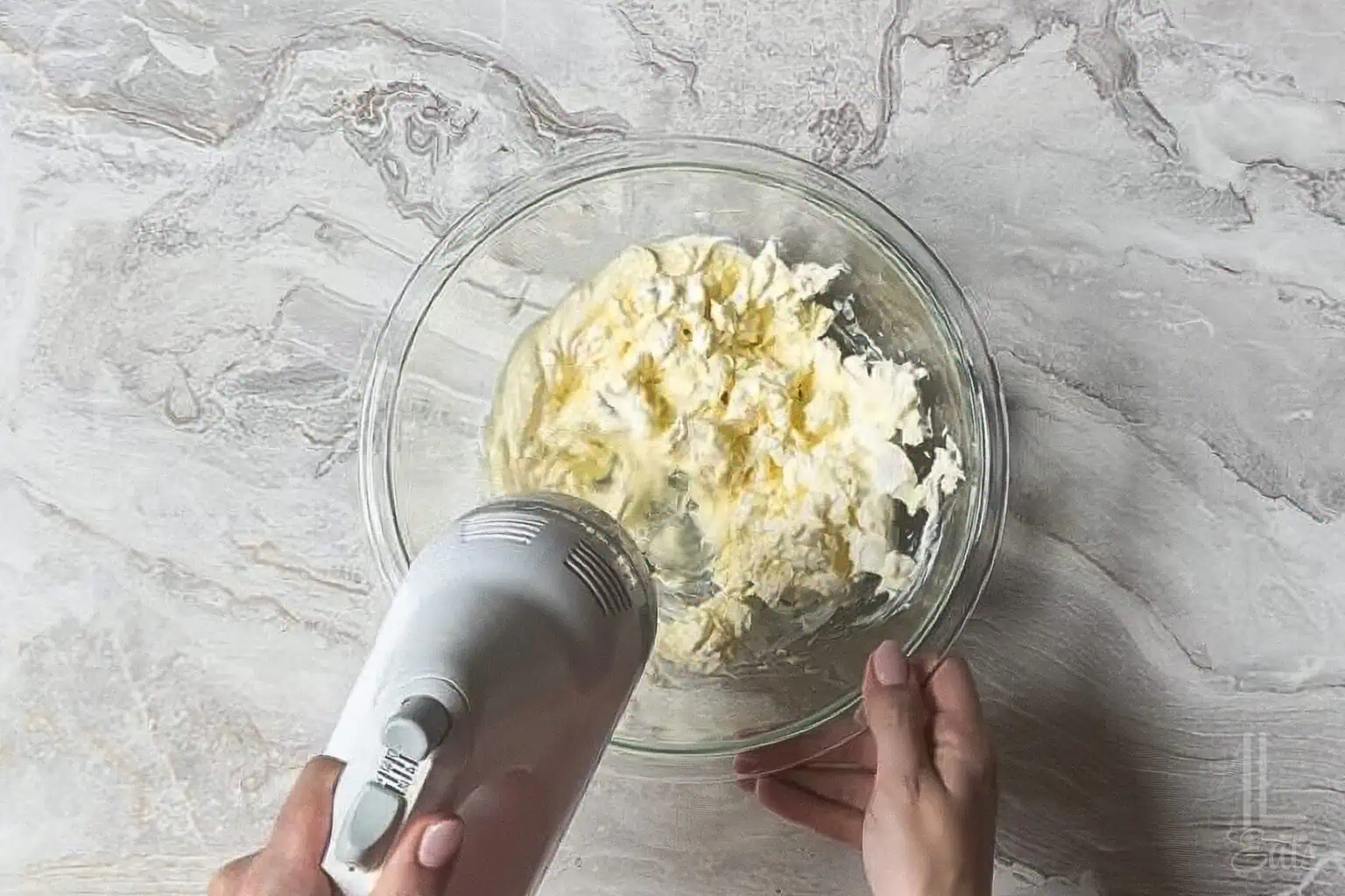 blending mayonnaise and cream cheese in a glass bowl with a hand mixer.