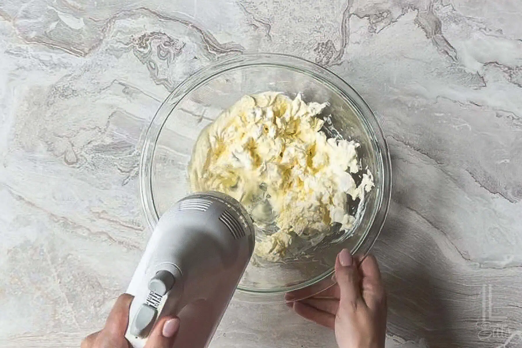 blending mayonnaise and cream cheese in a glass bowl with a hand mixer.
