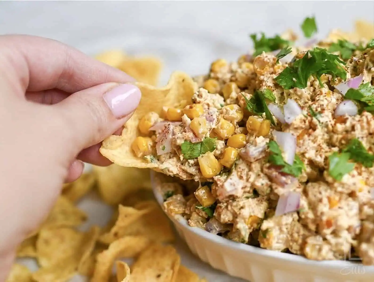 dipping a tortilla chip into the cold elote dip.