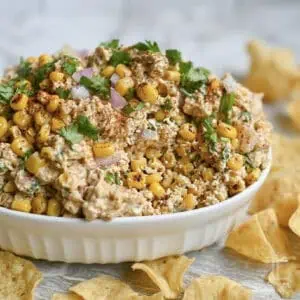 elote dip with corn, cilantro, and red onion in a serving dish, surrounded by tortilla chips.