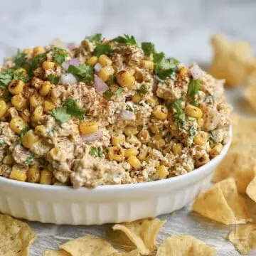 elote dip with corn, cilantro, and red onion in a serving dish, surrounded by tortilla chips.