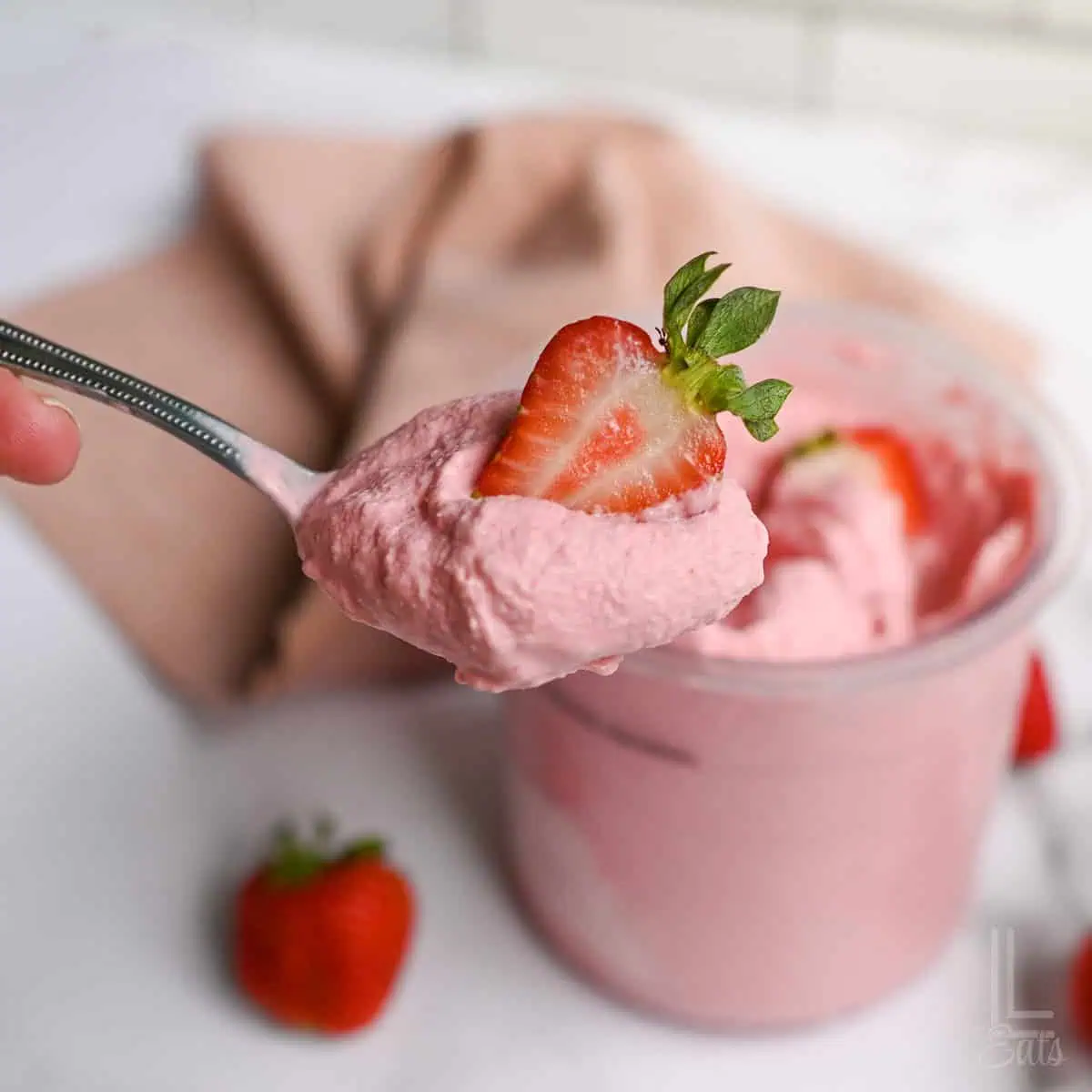 spoonful of strawberry ice cream topped with a strawberry slice, in front of a ninja creami container.