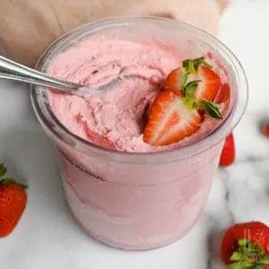 a container of ninja creami strawberry ice cream, topped with sliced strawberries.