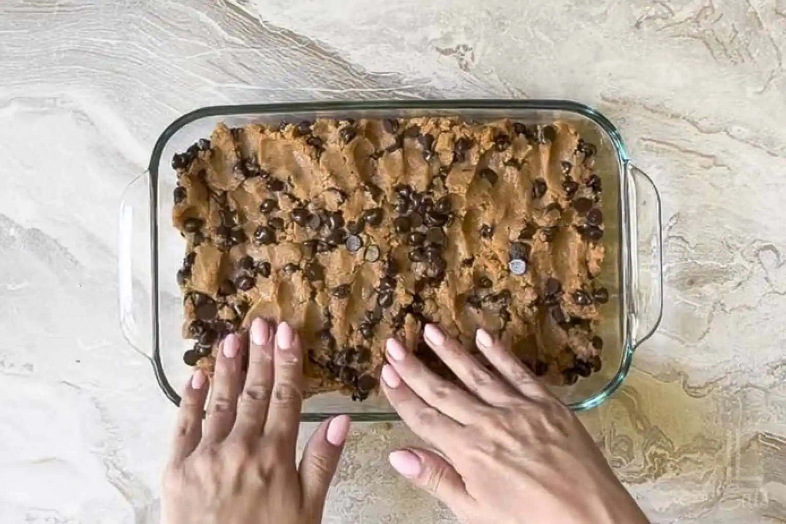 pressing the peanut butter cookie bar dough into a 7x11 inch pan with hands.