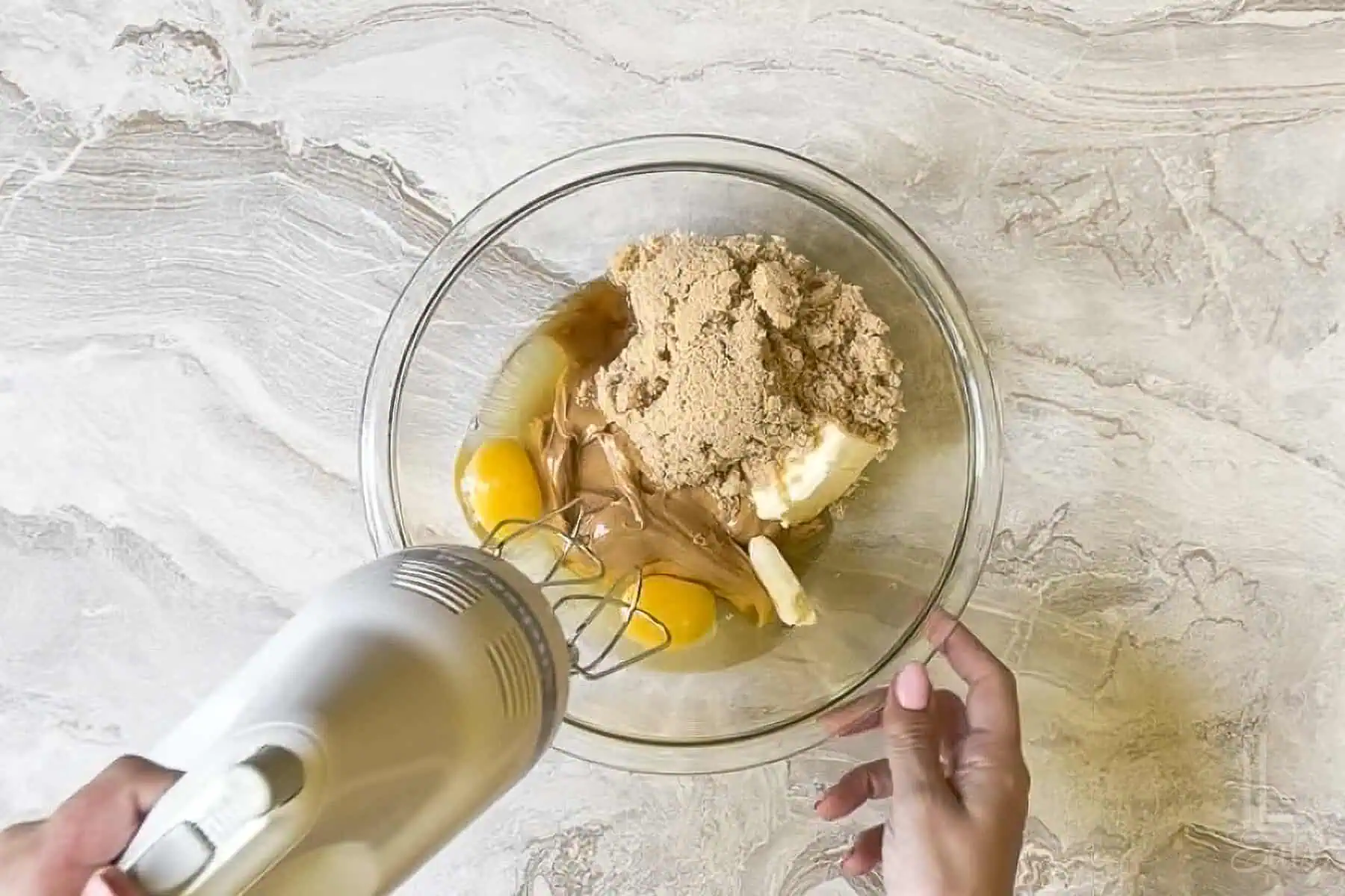 mixing wet ingredients (brown sugar, eggs, vanilla extract, butter) in a large glass bowl with a hand mixer.