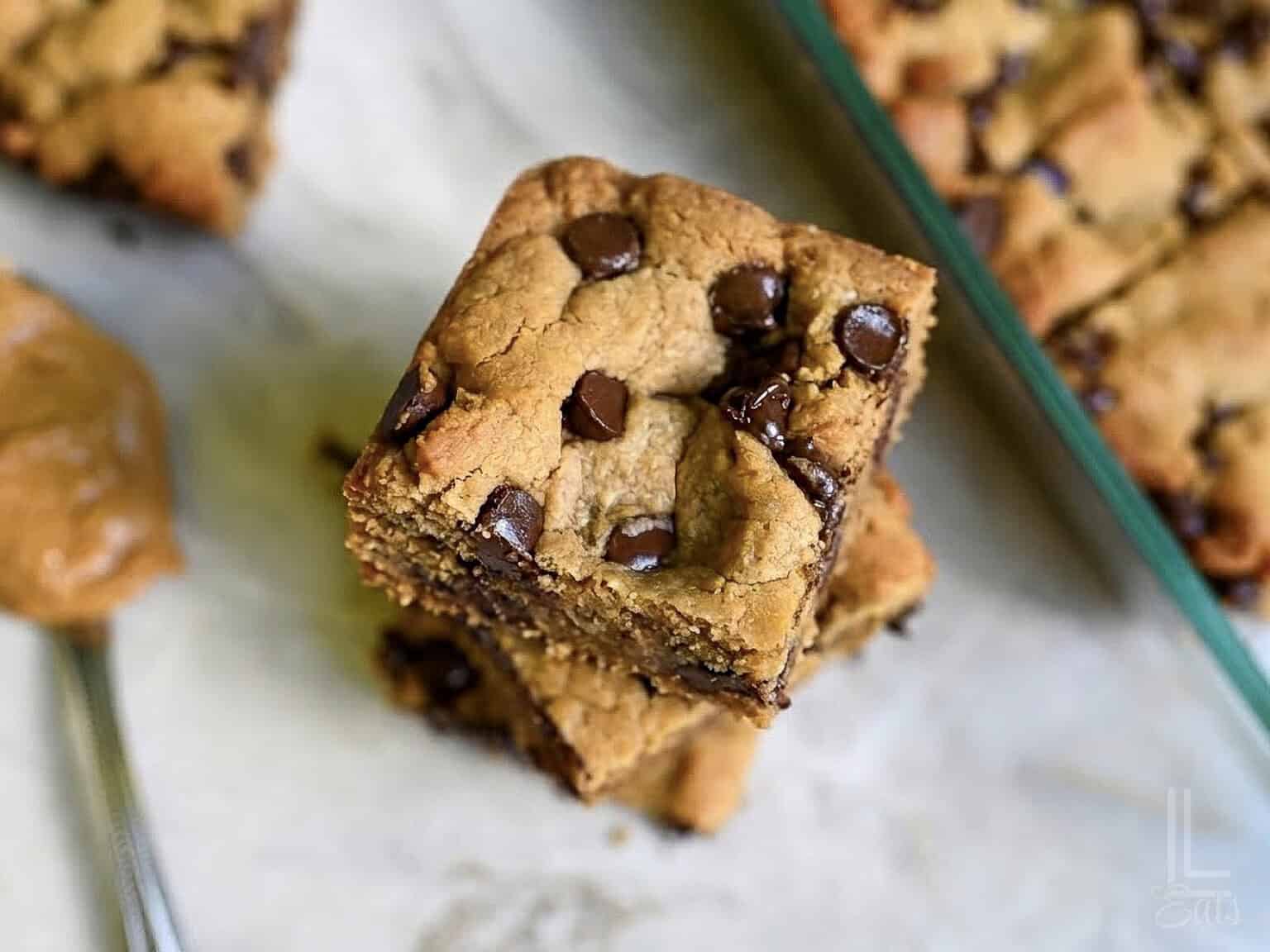 peanut butter cookie bars stacked next to a baking dish, showing melted chocolate chips.