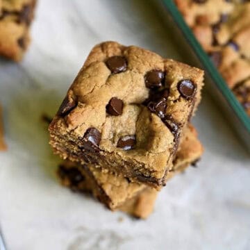 peanut butter cookie bars stacked next to a baking dish, showing melted chocolate chips.