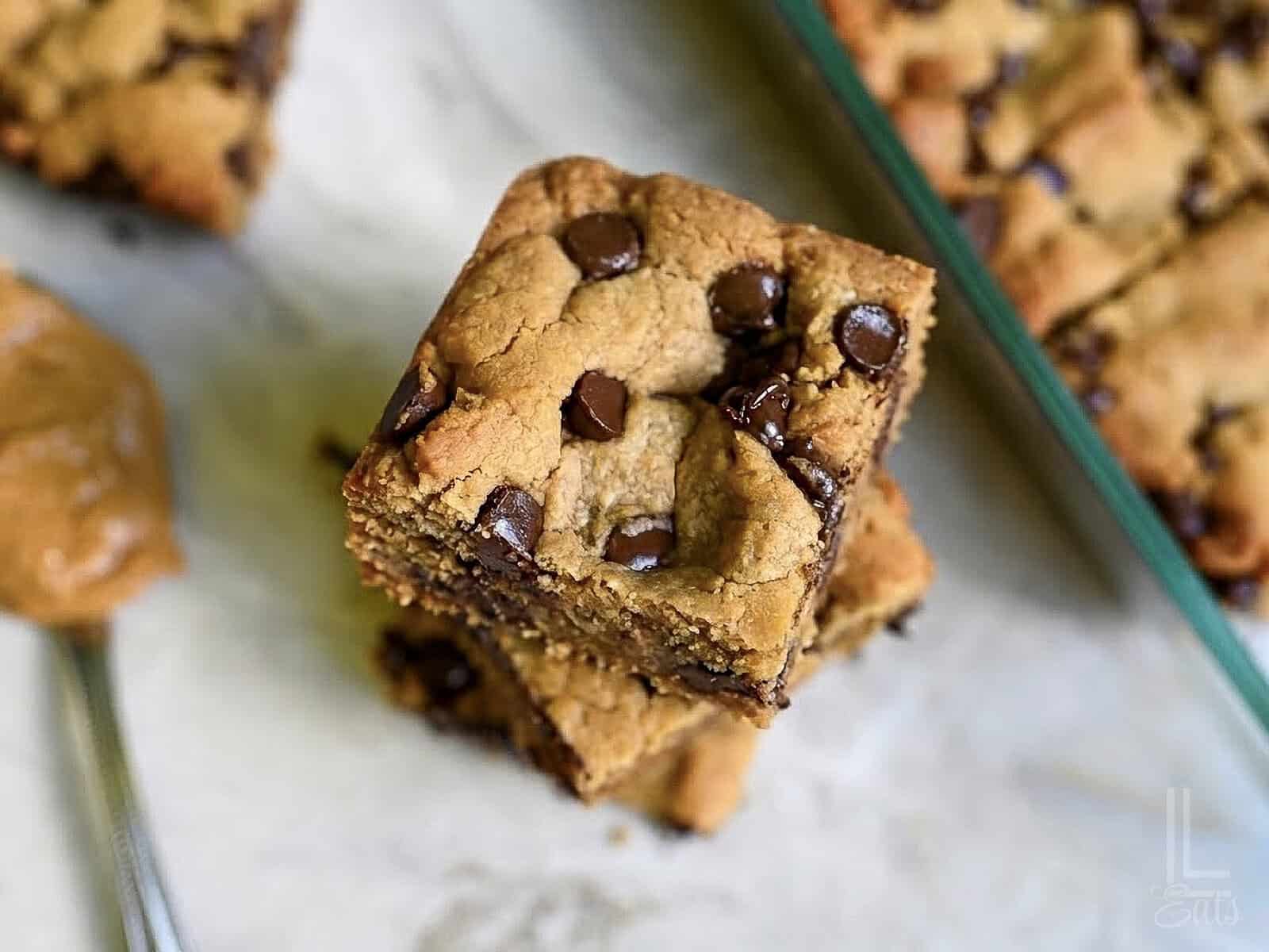 peanut butter cookie bars stacked next to a baking dish, showing melted chocolate chips.