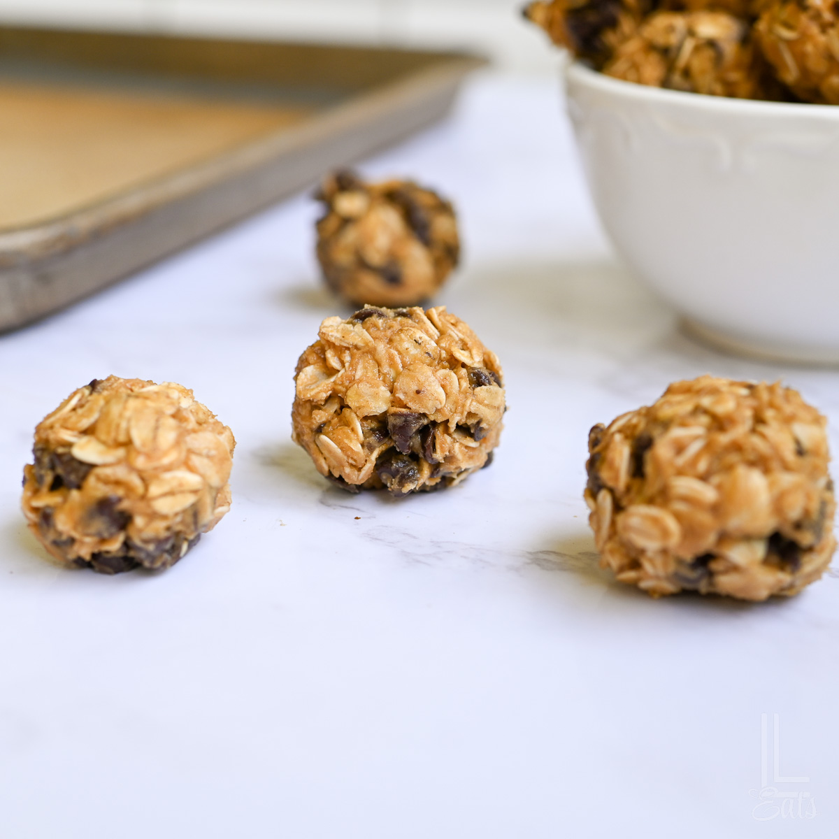 three peanut butter balls on a counter, with a bowl and baking sheet in the background.